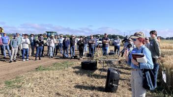 Crop-field demonstration: crowd, farming equipment, and a person holding a clipboard