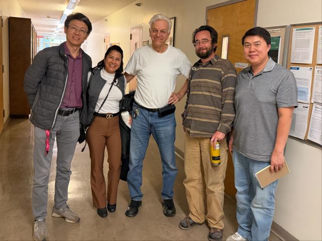 Five diverse individuals standing together in a hallway, smiling at the camera.